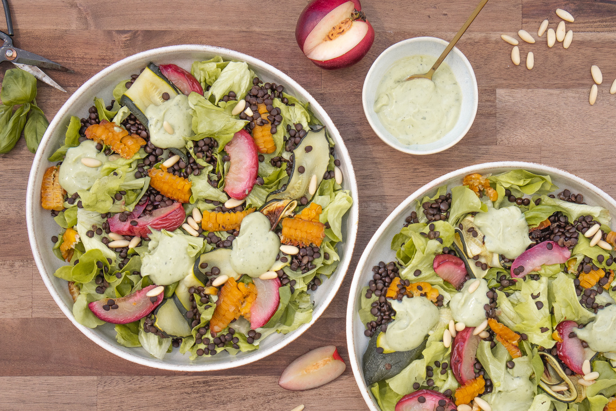 KI generiert: Das Bild zeigt eine Schüssel mit einem bunten Salat aus Rote-Bete-Scheiben, Karottenstreifen, Feldsalat, gehackten Nüssen und einem Klecks Sahne oder Joghurt in der Mitte. Der Salat liegt auf einem Holztisch.