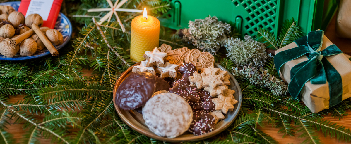 KI generiert: Teller mit Weihnachtsplätzchen, eine Kerze, Tannenzweige und Geschenkpäckchen in festlicher Dekoration.