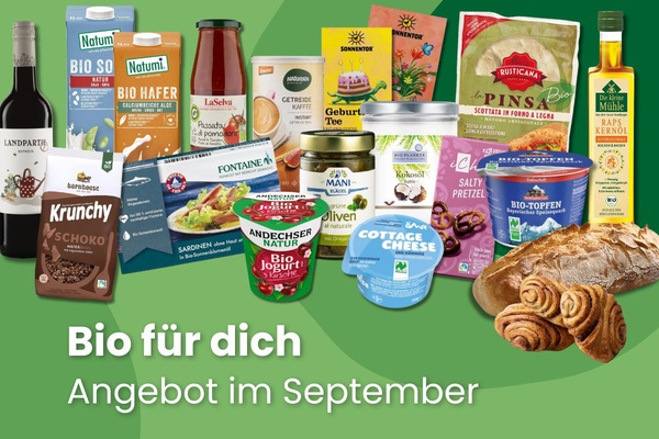 KI generiert: Das Bild zeigt zwei Personen in grüner Arbeitskleidung, die lächelnd eine Kiste mit frischem Obst und Gemüse halten. Im Hintergrund sind weitere Kisten mit Tomaten, Äpfeln und Salat zu sehen, was auf ein Lager oder eine Verkaufsstelle für frische Lebensmittel hinweist.