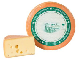 KI generiert: Ein runder Laib Käse mit einem Stück abgeschnitten. Aufschrift: "Allgäuer Glosamomente Bio Weichkäse".