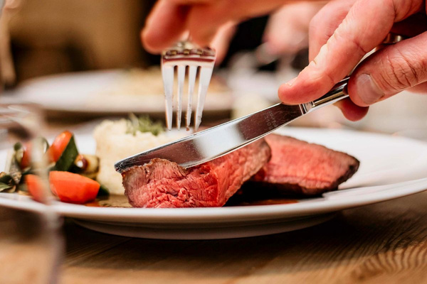 KI generiert: Ein saftiges Steak wird mit Messer und Gabel auf einem Teller geschnitten.