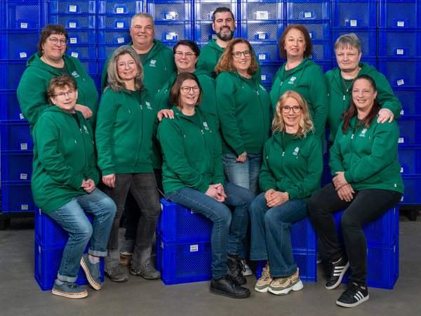 KI generiert: Eine Gruppe von Personen in grünen Hoodies sitzt und steht vor blauen Kisten.