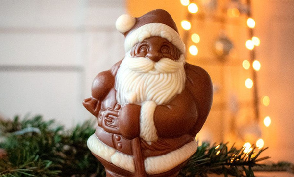 KI generiert: Schokoladen-Weihnachtsmann auf Tannenzweigen, im Hintergrund verschwommene Lichter.