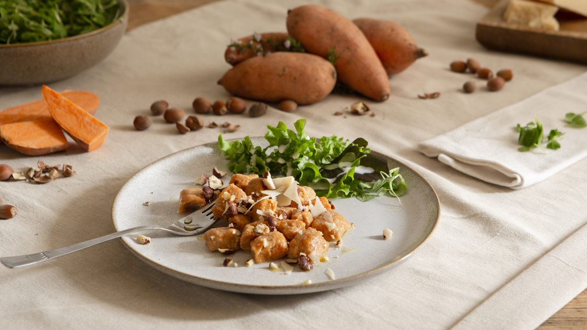 KI generiert: Das Bild zeigt eine Schüssel mit einem bunten Salat aus Rote-Bete-Scheiben, Karottenstreifen, Feldsalat, gehackten Nüssen und einem Klecks Sahne oder Joghurt in der Mitte. Der Salat liegt auf einem Holztisch.