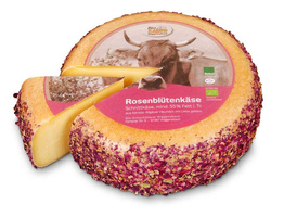 KI generiert: Ein runder Käse mit Rosenblüten, ein Stück herausgeschnitten. Text: "Rosenblütenkäse, mind. 55% Fett i. Tr."