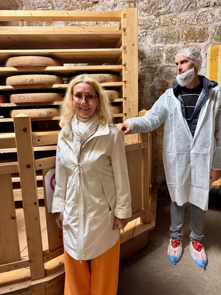 KI generiert: Zwei Personen in einem Käsekeller, umgeben von großen Käserädern auf Regalen. Keine sichtbaren Texte.