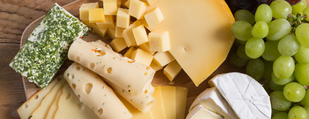 KI generiert: Verschiedene Käsesorten und grüne Trauben auf einem Holzbrett.