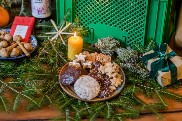 KI generiert: Weihnachtliche Kekse und Geschenk umgeben von Tannenzweigen und einer Kerze auf einem Tisch.