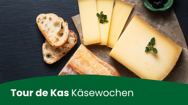 KI-generierte Beschreibung: Tour de Kas Käsewochen: Käsestücke und Kräuter auf Holzbrett.