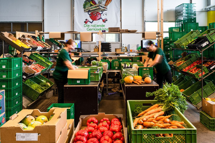 KI generiert: Angestellte packen frisches Gemüse in Kisten. Text: "Die rollende Gemüsekiste".