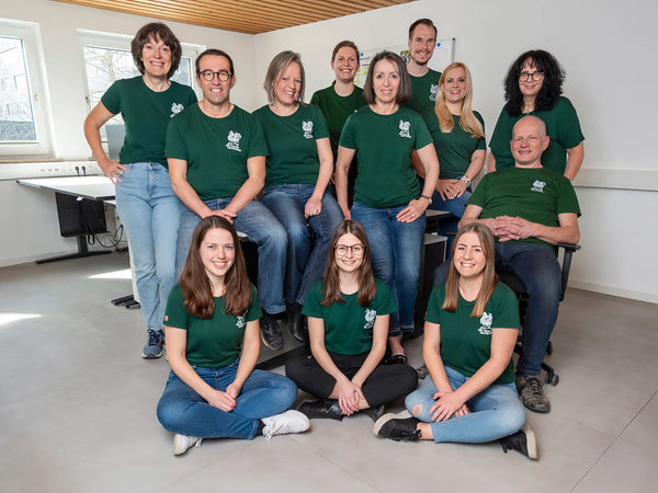 KI generiert: Eine Gruppe von 12 Personen in grünen T-Shirts posiert zusammen in einem Raum.