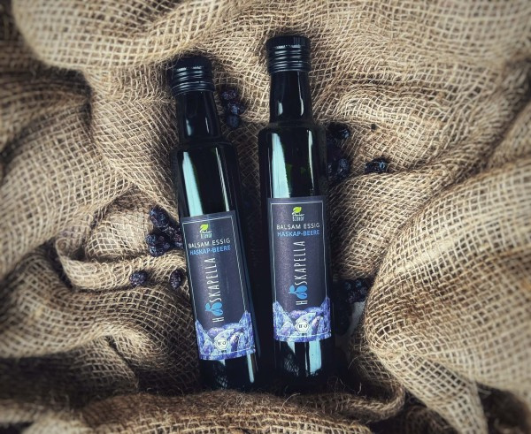 KI generiert: Zwei Flaschen Balsamico-Essig "Haskap-Beere" auf Jute. Text: "BALSAM ESSIG HASKAP-BEERE"