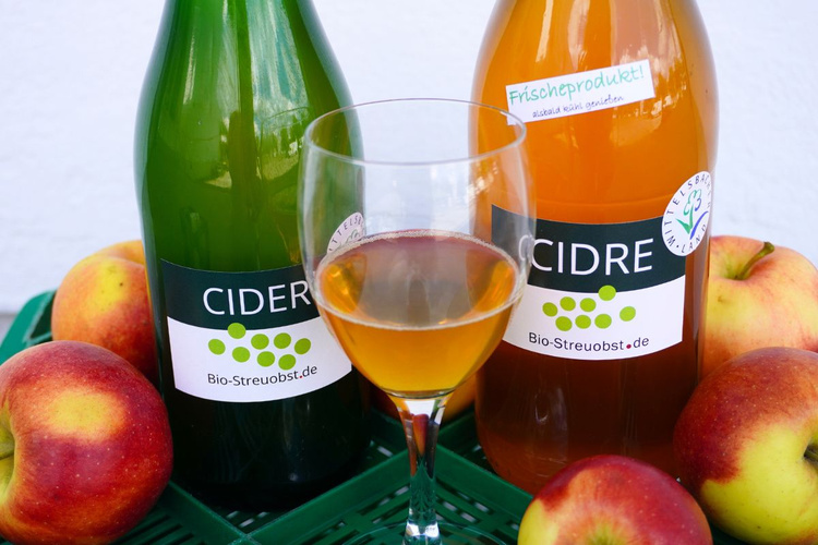 KI generiert: Zwei Flaschen Cidre und ein Glas mit Apfelsaft, umgeben von Äpfeln. Text: "Bio-Streuobst.de, Frischeprodukt!"
