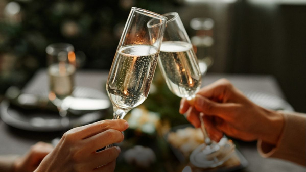 KI generiert: Zwei Menschen stoßen mit Sektgläsern an, im Hintergrund ein gedeckter Tisch.