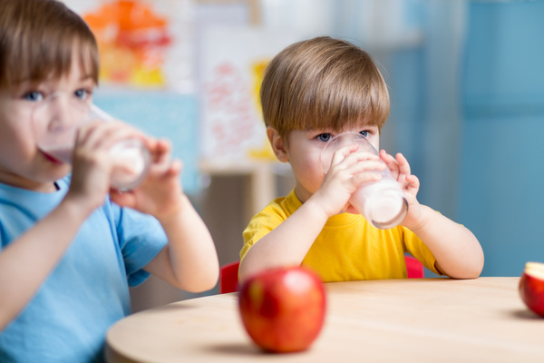 KI generiert: Zwei Kinder trinken Milch, während ein Apfel auf dem Tisch liegt.