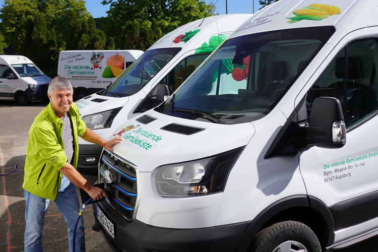 KI generiert: Ein Mann lädt ein Elektrofahrzeug mit dem Logo "Die rollende Gemüsekiste GmbH" auf.