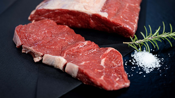 KI generiert: Rohes Rindfleisch auf schwarzem Untergrund mit Meersalz und einem Rosmarinzweig.