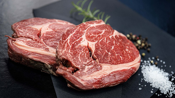 KI generiert: Zwei rohe Ribeye-Steaks auf einem schwarzen Untergrund mit Rosmarin, Pfefferkörnern und Salz.