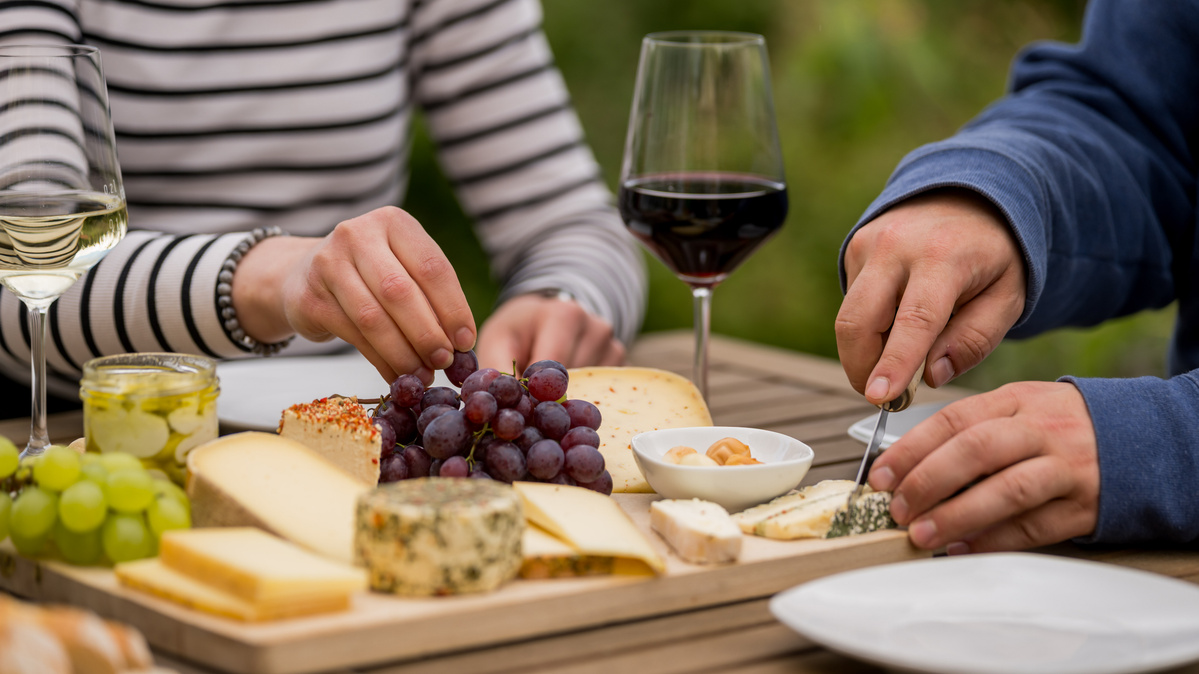 KI generiert: Eine Käseplatte mit Trauben und zwei Gläsern Wein auf einem Holztisch.