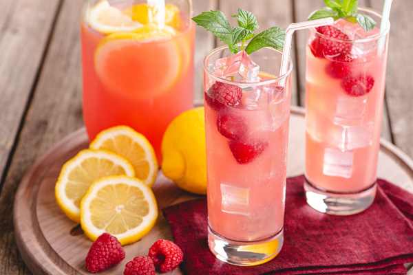 KI generiert: Das Bild zeigt zwei Personen in grüner Arbeitskleidung, die lächelnd eine Kiste mit frischem Obst und Gemüse halten. Im Hintergrund sind weitere Kisten mit Tomaten, Äpfeln und Salat zu sehen, was auf ein Lager oder eine Verkaufsstelle für frische Lebensmittel hinweist.