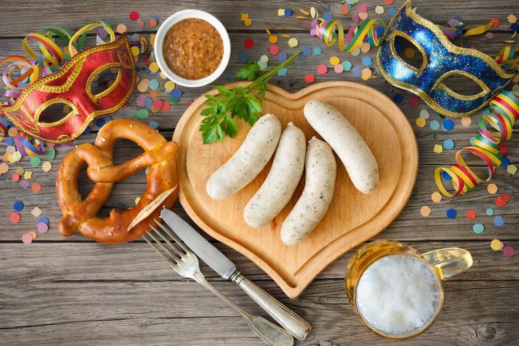 KI generiert: Kulinarische Tischdekoration mit Weißwürsten, Brezel, Bier, Senf, Masken und Konfetti auf Holz.