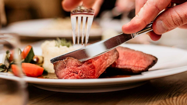 KI generiert: Jemand schneidet ein Stück rosa gebratenes Fleisch auf einem Teller mit Gemüse an.