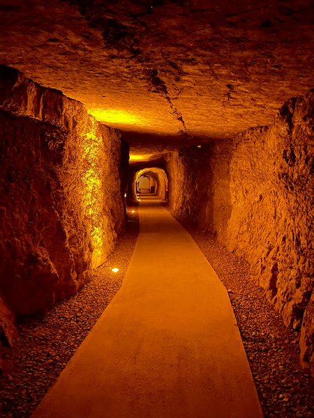 KI generiert: Ein beleuchteter, in warmem Licht gehaltener Tunnel aus Naturstein.