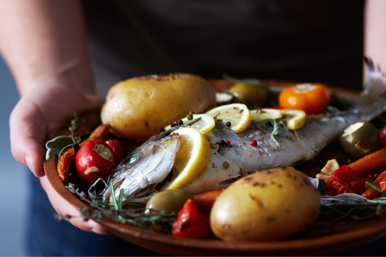 KI generiert: Ein gebackener Fisch mit Zitronenscheiben, Kartoffeln und Gemüse auf einem Teller.