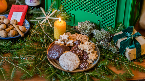 KI generiert: Teller mit Weihnachtsplätzchen und Kerze auf Tannengrün, neben Walnüssen und Geschenk.