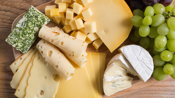 KI generiert: Verschiedene Käsesorten und grüne Trauben auf einem Holzbrett.