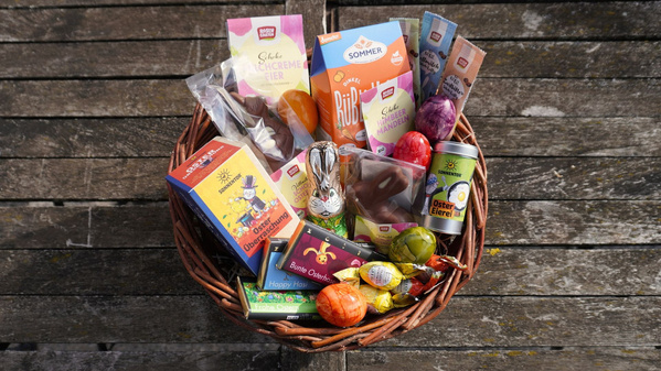 KI generiert: Ein Geschenkkorb voller Osterprodukte und Schokolade, darunter ein Schoko-Osterhase und bunte Eier.