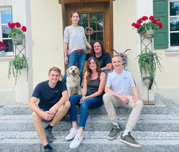 KI generiert: Eine Gruppe von fünf Personen und ein Hund sitzen auf Stufen vor einem Haus. Text: "2006 Familie BZ3".