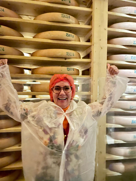 KI generiert: Eine Person in Schutzkleidung posiert vor einer Wand mit großen Käseleibern. Text: "151024".