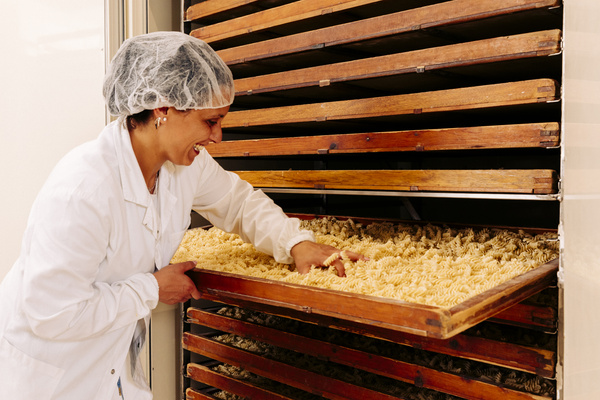 KI generiert: Eine Person überprüft trocknende Nudeln auf Holztabletts in einem Produktionsbereich.