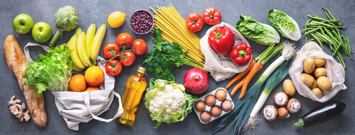 KI generiert: Verschiedene frische Lebensmittel, darunter Obst, Gemüse, Nudeln und Brot, auf einem grauen Hintergrund drapiert.