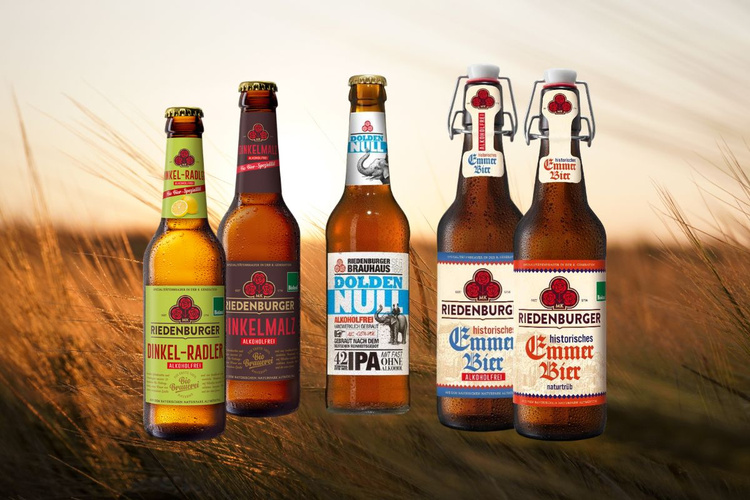 KI generiert: Fünf Riedenburger Bierflaschen in einem Feld. Texte: „Dinkel-Radler“, „Dinkelmalz“, „Dolden Null“, „Emmer Bier“.