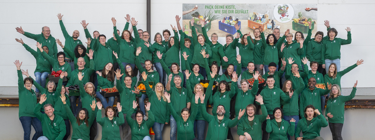 KI generiert: Eine Gruppe von Menschen in grünen Hoodies posiert freudig zusammen. Text: "PACK DEINE KISTE, WIE SIE DIR GEFÄLLT."