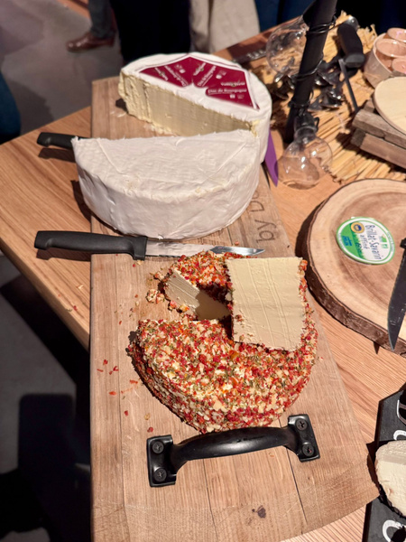 KI generiert: Ein Tisch mit verschiedenen Käsesorten, darunter ein Käse mit Paprikaüberzug und ein Brie-Käse.