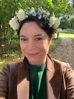 KI generiert: Eine lächelnde Person mit Blumenkranz im Haar in einem Garten.