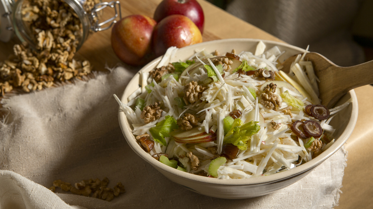 KI generiert: Das Bild zeigt eine Schüssel mit einem bunten Salat aus Rote-Bete-Scheiben, Karottenstreifen, Feldsalat, gehackten Nüssen und einem Klecks Sahne oder Joghurt in der Mitte. Der Salat liegt auf einem Holztisch.