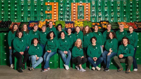 KI generiert: Gruppe von Personen in grüner Arbeitskleidung vor Kisten mit Obst und Gemüse.