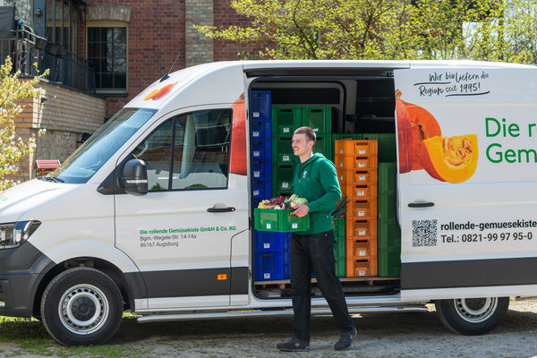 KI generiert: Ein Lieferwagen mit Gemüsekisten; ein Mann trägt eine Kiste. Text: "rollende-gemuesekiste.de" und Telefonnummern.
