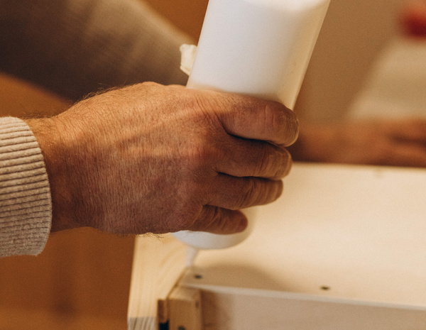 KI generiert: Eine Hand trägt Leim auf ein Holzstück auf.