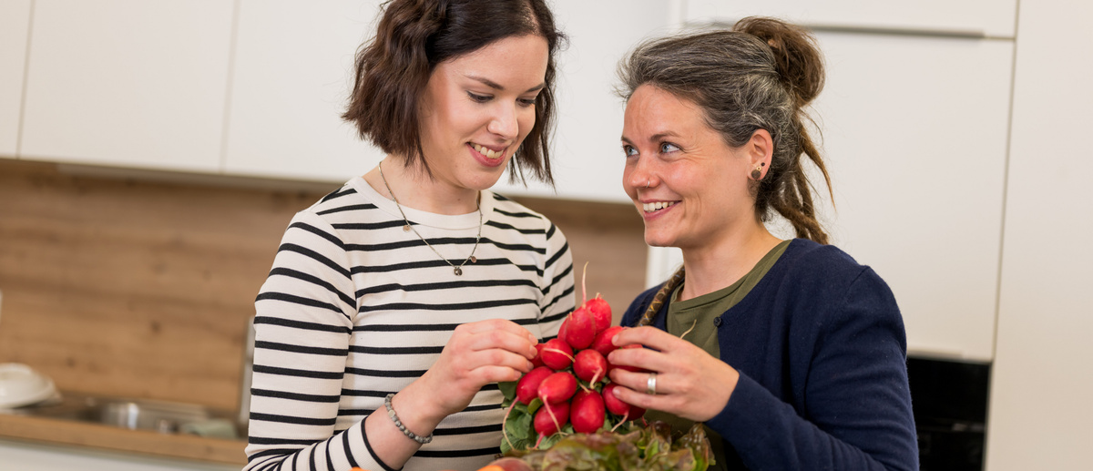 KI generiert: Zwei Frauen stehen in einer Küche und halten einen Bund Radieschen.
