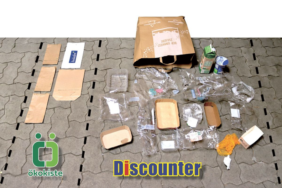 KI generiert: Papier- und Plastikverpackungen auf Boden verteilt, Text: "Discounter", "ökokiste".