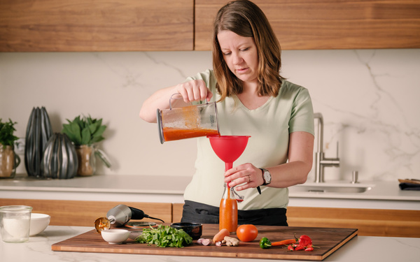 KI generiert: Eine Frau füllt Tomatensauce mit einem Trichter in eine Flasche.