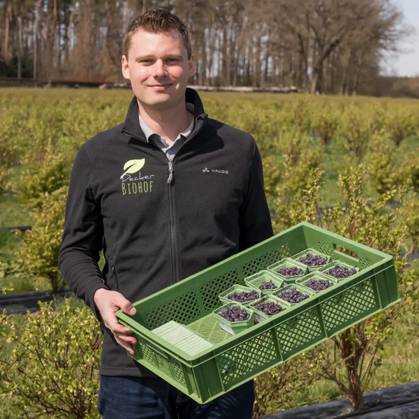 KI generiert: Ein Mann hält eine Kiste mit gepflückten Beeren. Auf seiner Jacke steht "Becker Biohof".