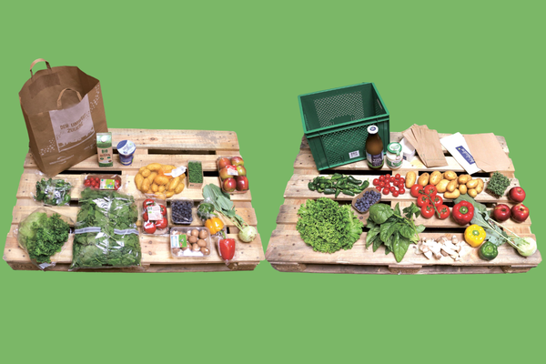 KI generiert: Das Bild zeigt zwei Personen in grüner Arbeitskleidung, die lächelnd eine Kiste mit frischem Obst und Gemüse halten. Im Hintergrund sind weitere Kisten mit Tomaten, Äpfeln und Salat zu sehen, was auf ein Lager oder eine Verkaufsstelle für frische Lebensmittel hinweist.