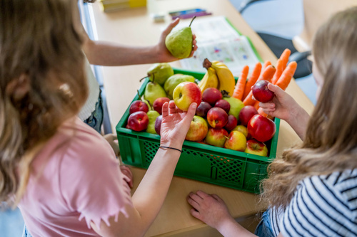 KI generiert: Kinder untersuchen eine Kiste mit frischem Obst und Gemüse auf einem Tisch.