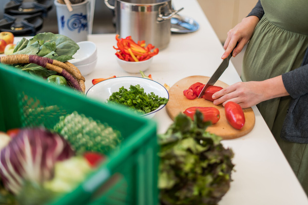 KI generiert: Jemand schneidet rote Paprika in einer Küche, umgeben von frischem Gemüse.